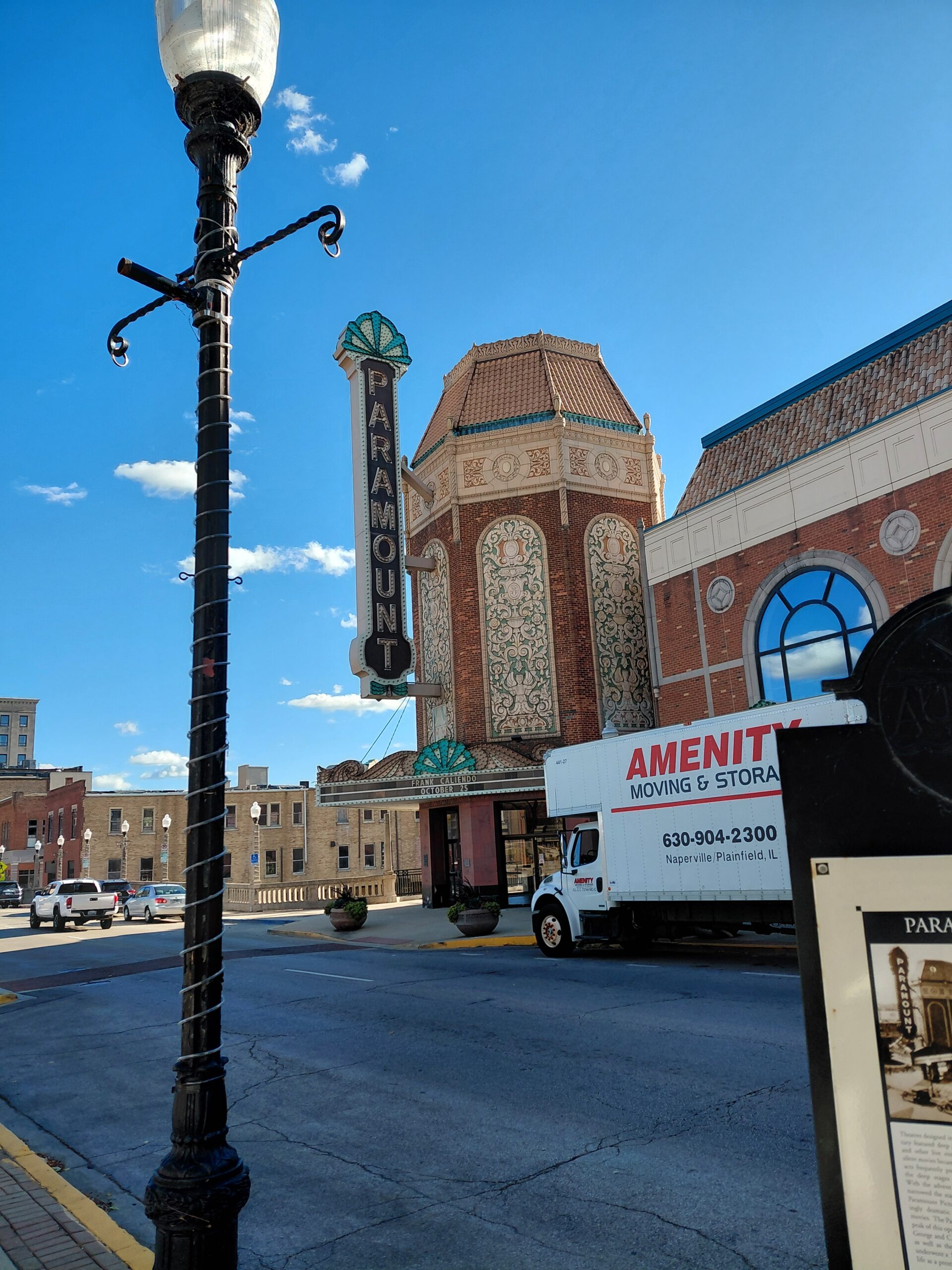 Paramount Theatre’s iconic marquee stands tall against a clear blue sky. A moving truck is parked nearby, highlighting the venue's lively surroundings.